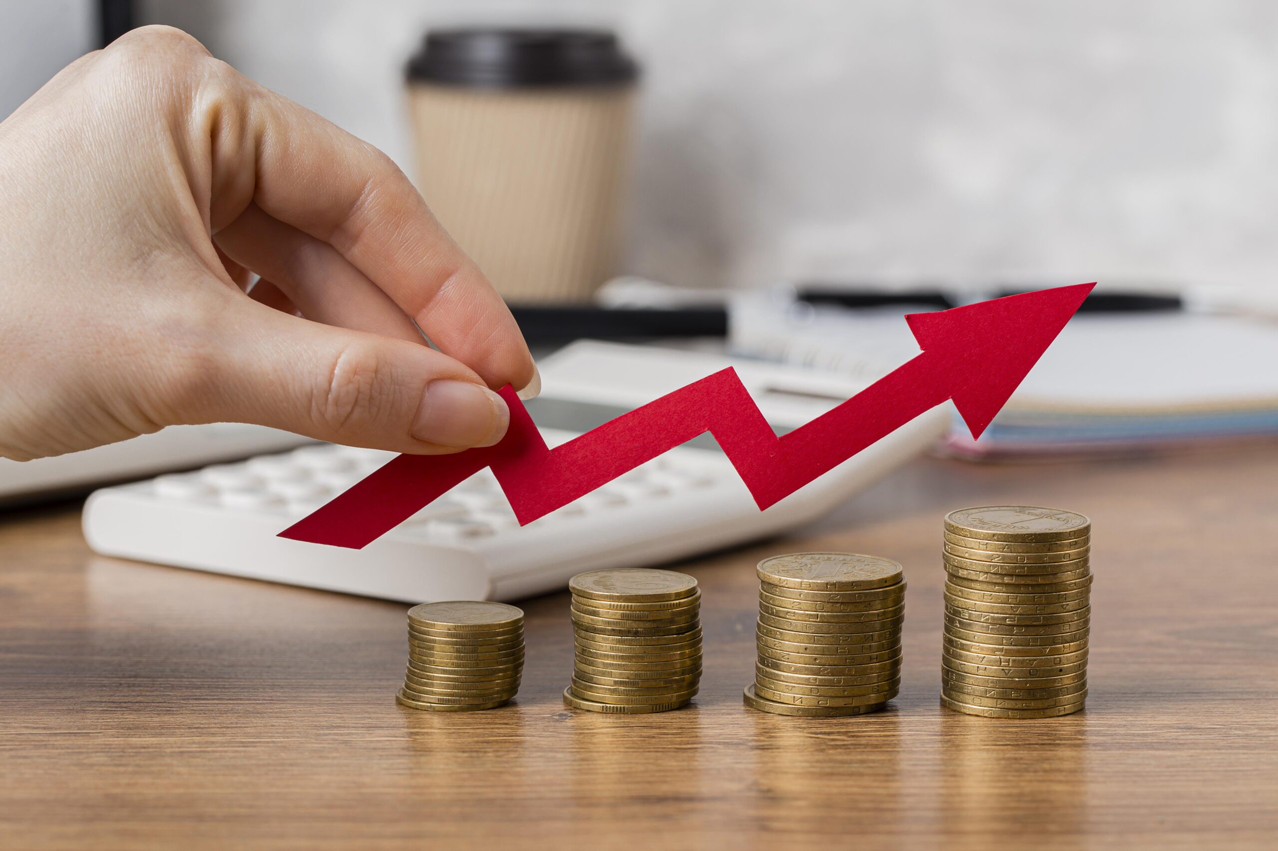 The image shows a person's hand holding a red upward trending arrow graph over stacks of gold coins that increase in height from left to right, symbolizing investment growth. In the background, there's a calculator representing financial planning and analysis. This visual effectively illustrates the concept of investment thresholds and financial growth relevant to the article about PPLI (Private Placement Life Insurance) minimum investment requirements